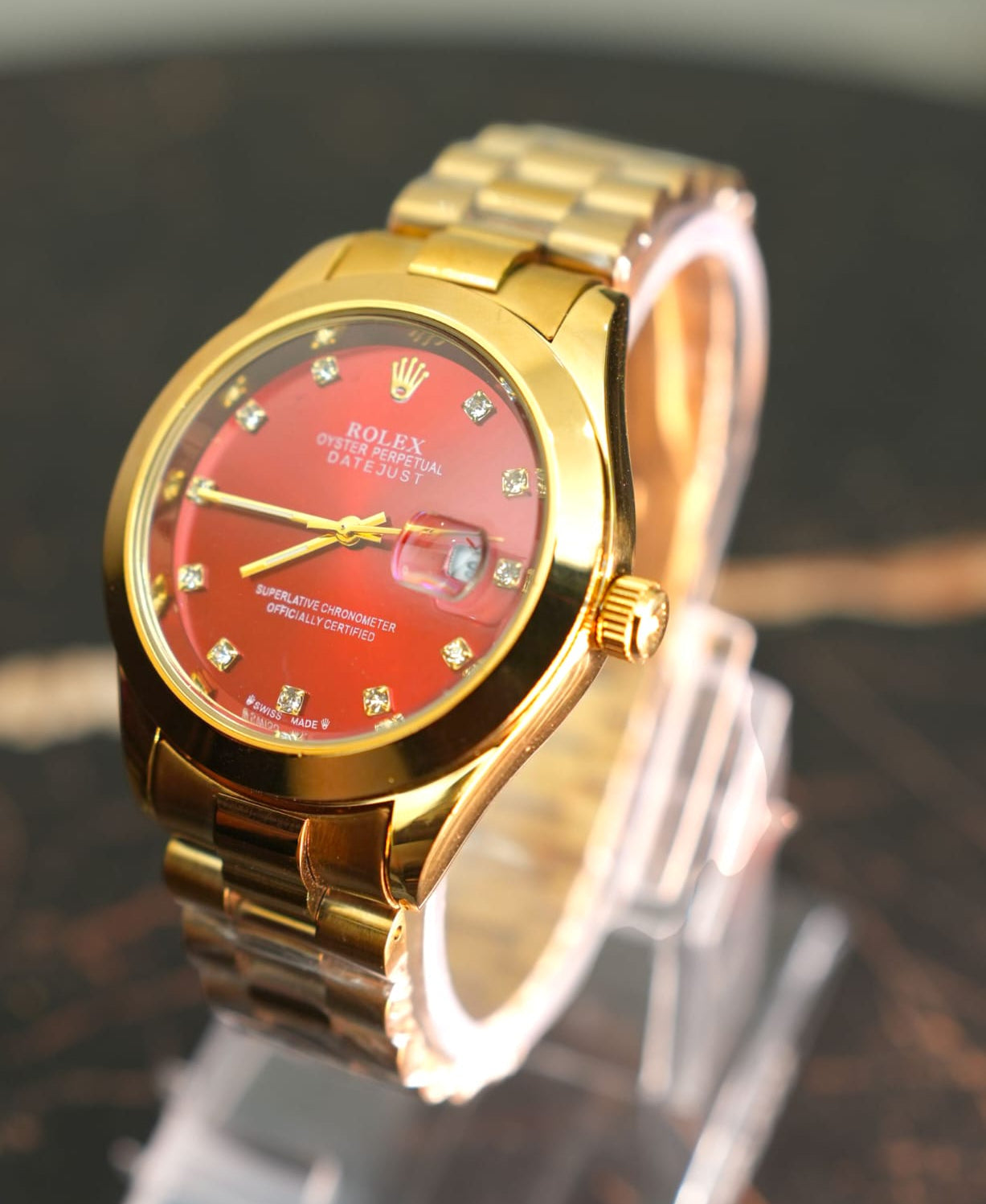 Gold rolex watch with a red dial on a reflective surface